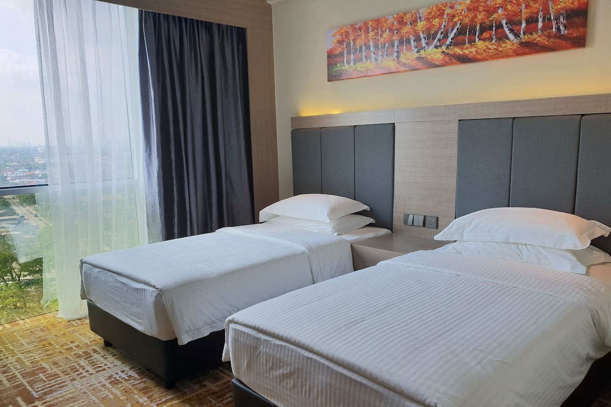 A hotel room with two beds, a large window with curtains, a painting of autumn trees, and a city view.