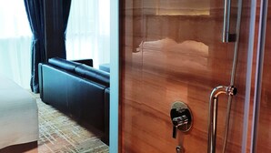 A hotel room with a wooden door, a shower with a handheld showerhead, a black leather sofa, and a patterned rug. - KSL Hot Spring Resort (Johor Bahru)