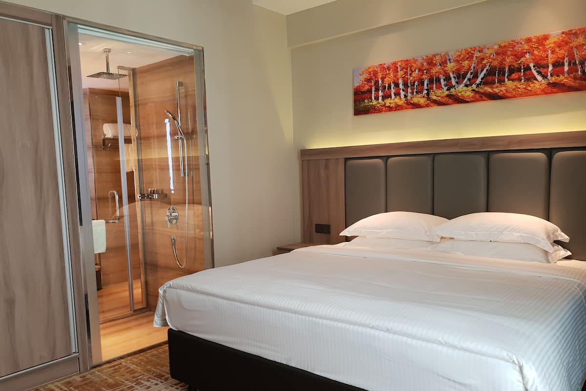 A hotel room with a bed, a shower, and a painting of autumn leaves on the wall.
