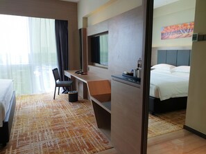 Quarto de hotel com cama, escrivaninha, cadeira, televisão e janela com cortinas.
