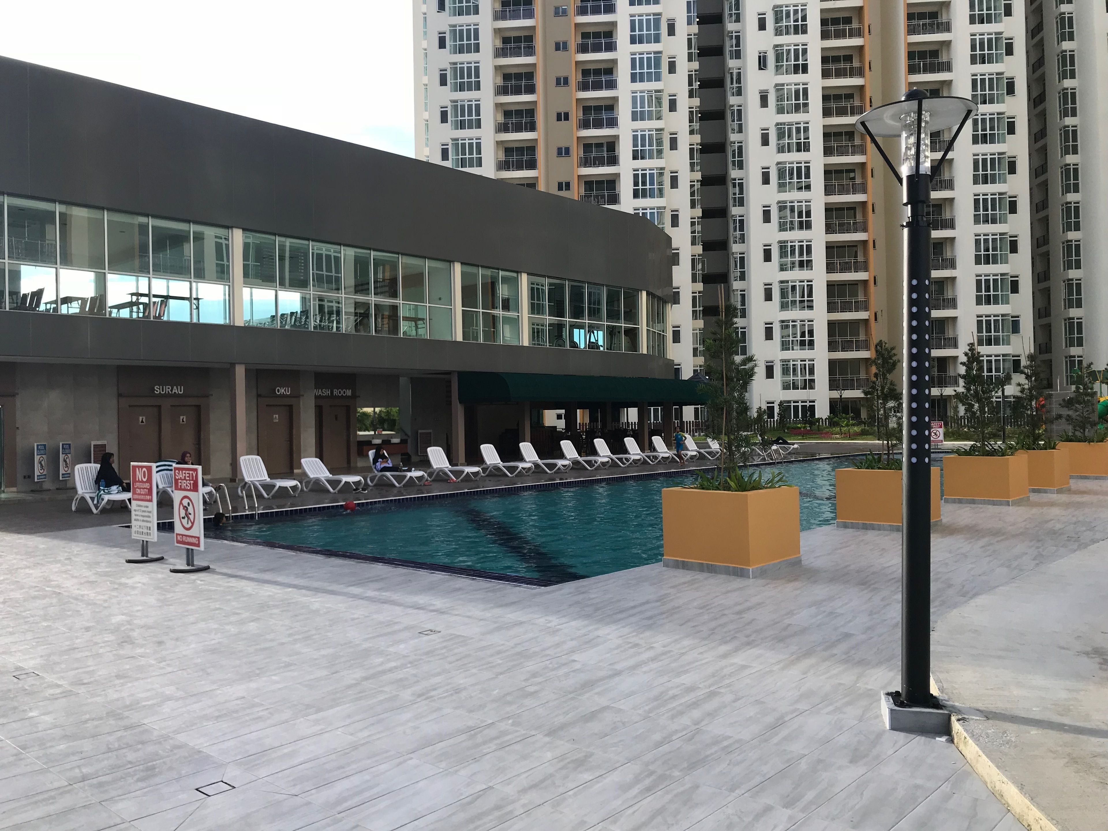 Un hotel moderno con piscina, sillas de descanso y un cartel de seguridad.