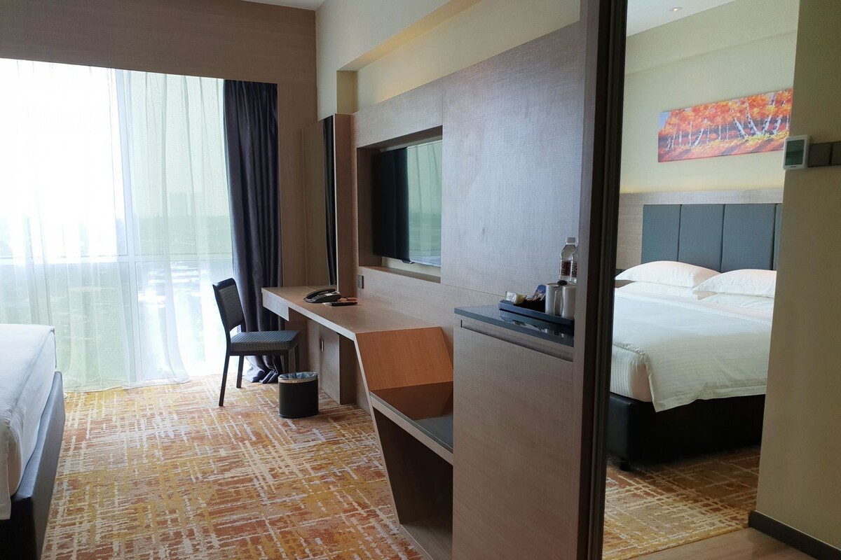 Une chambre d’hôtel avec un lit, un bureau, une chaise, une télévision et une fenêtre avec des rideaux.