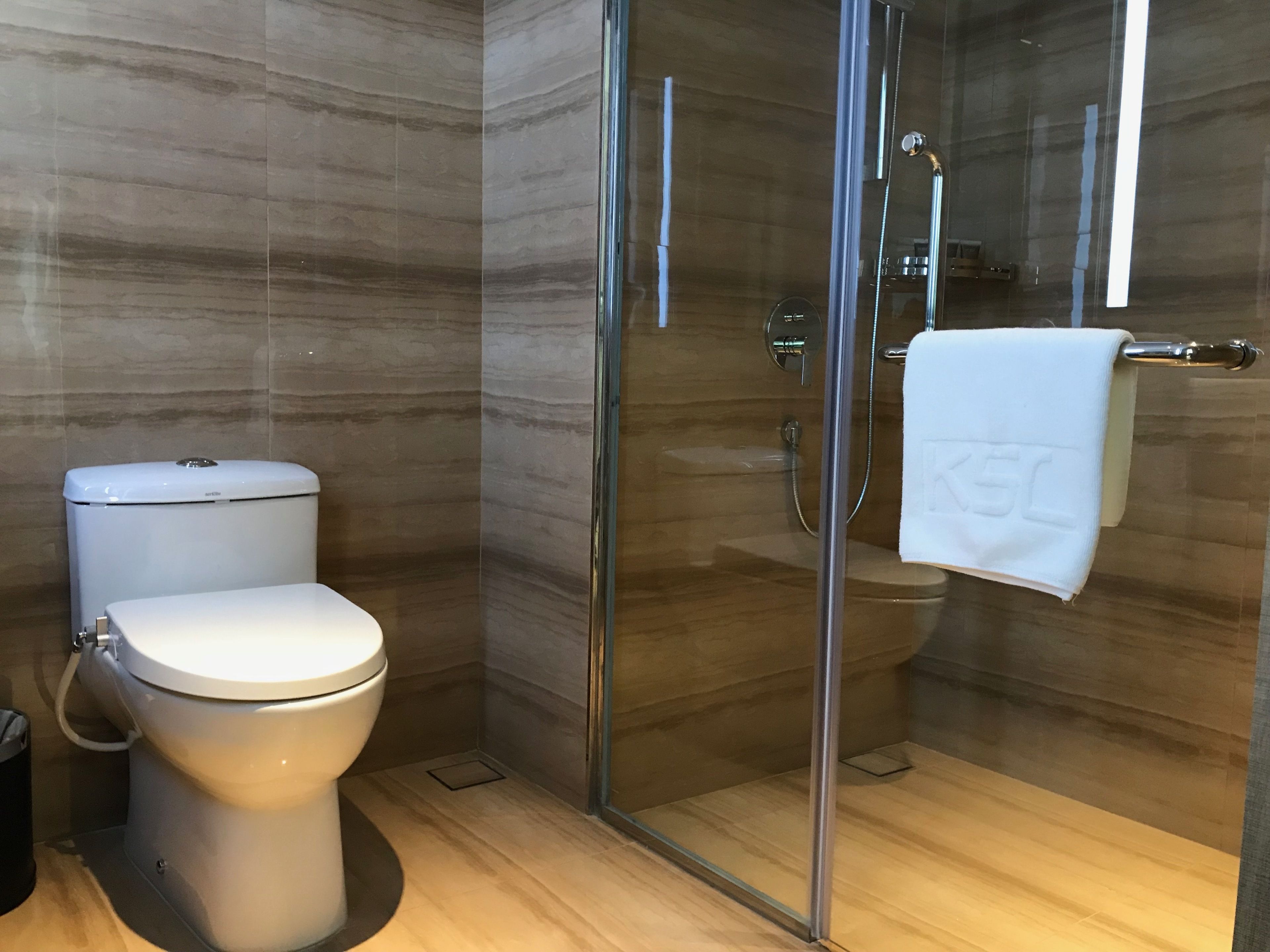 A modern bathroom with a toilet, a glass-enclosed shower, and a towel hanging on a rack.
