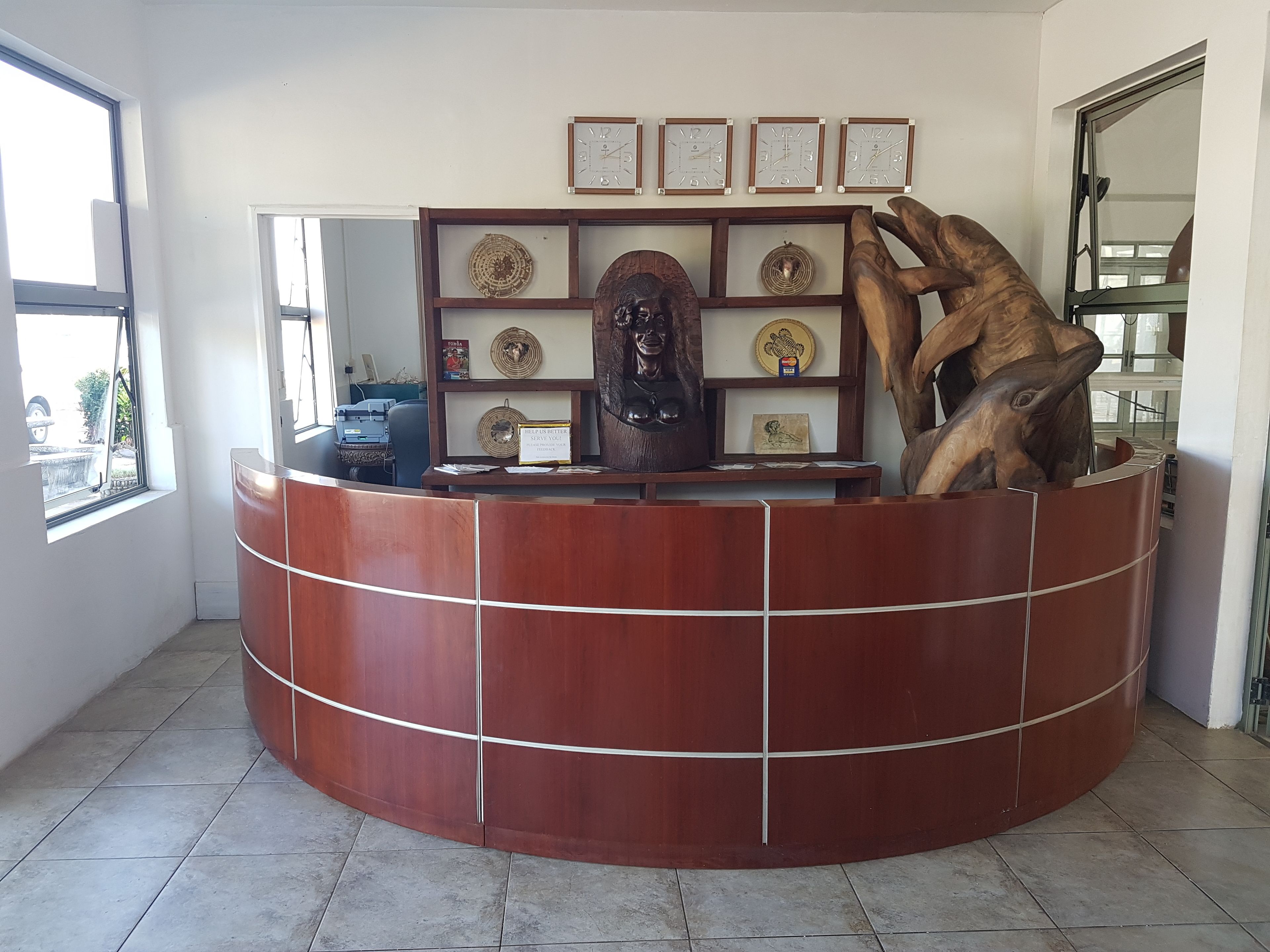 A reception desk with a wooden finish, a wall-mounted clock, and a decorative wooden sculpture.