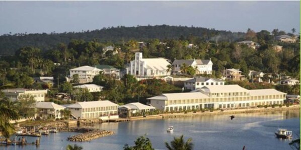 A coastal town with a large white building, possibly a hotel, near a body of water with boats. - Puataukanave International Hotel (Neiafu)