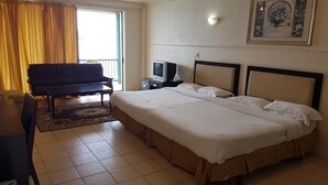 Een hotelkamer met een groot bed, een bank, een televisie en een balkon met gordijnen.
