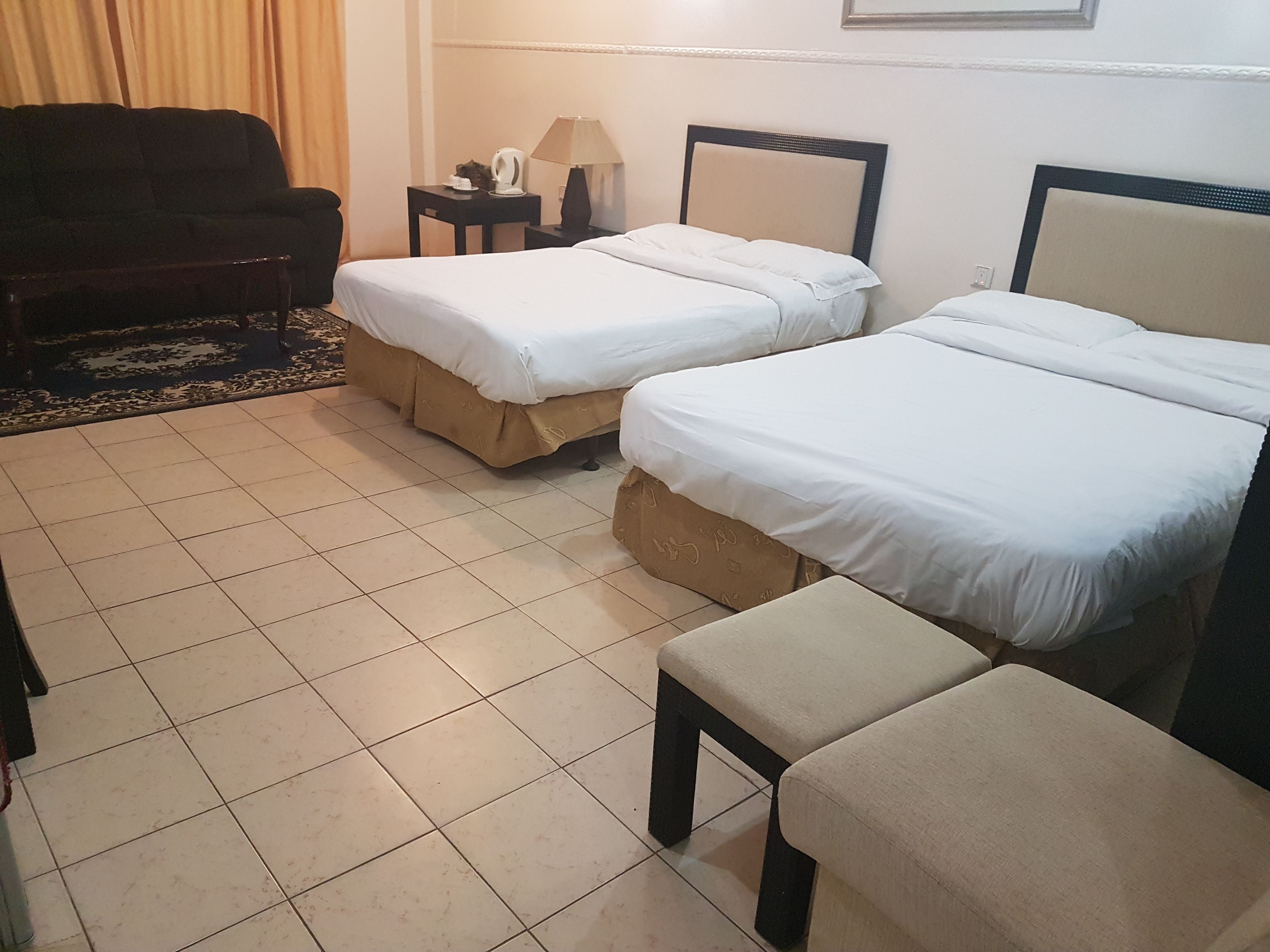 A hotel room with two single beds, a sofa, a small table with a lamp, and a chair.