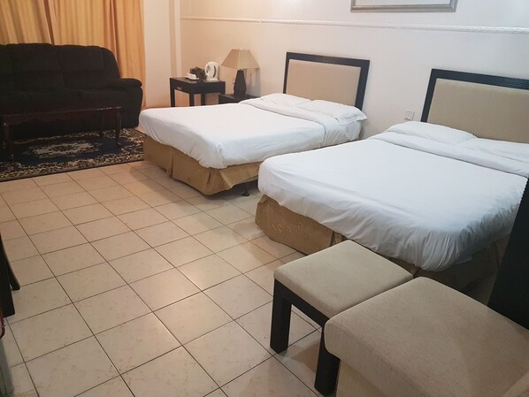 A hotel room with two single beds, a sofa, a small table with a lamp, and a chair.