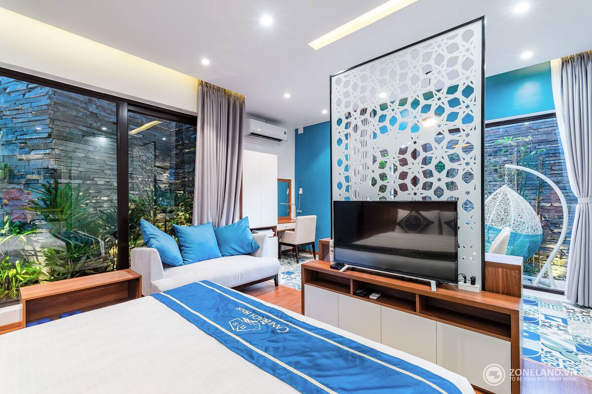A modern hotel room with a large bed, a TV, a seating area, and a view of the outdoors.