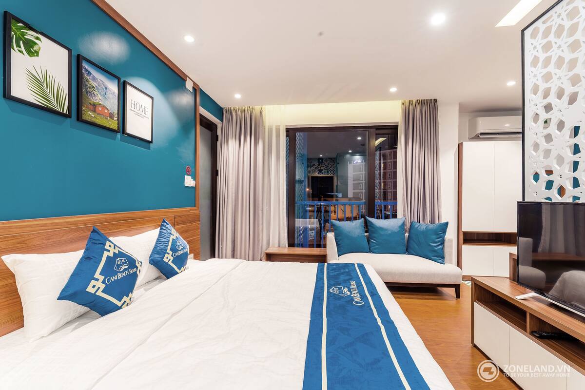 A hotel room with a bed, a sofa, a TV, and a balcony with curtains.