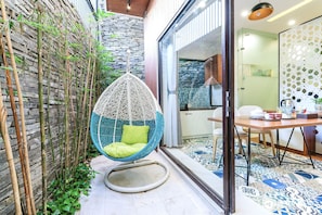Une chaise suspendue avec un coussin vert, un mur en pierre et un sol carrelé.