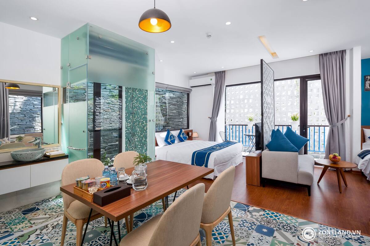 A modern hotel room with a bed, sofa, dining table, and a balcony with a view.