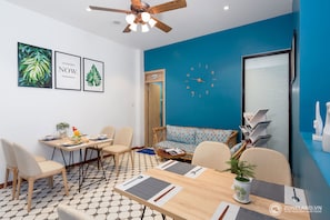 Une pièce moderne avec un mur d’accent bleu, une table à manger en bois, des chaises, un canapé, une horloge et des œuvres d’art encadrées.