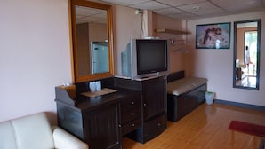 Une pièce avec un grand miroir, un téléviseur posé sur un meuble, un lit, une commode et une petite fenêtre.