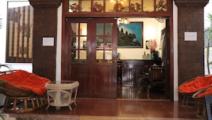 A reception area with a wooden door, wicker chairs, and a painting on the wall. - Angkor Sangrith Hostel (Siem Reap)