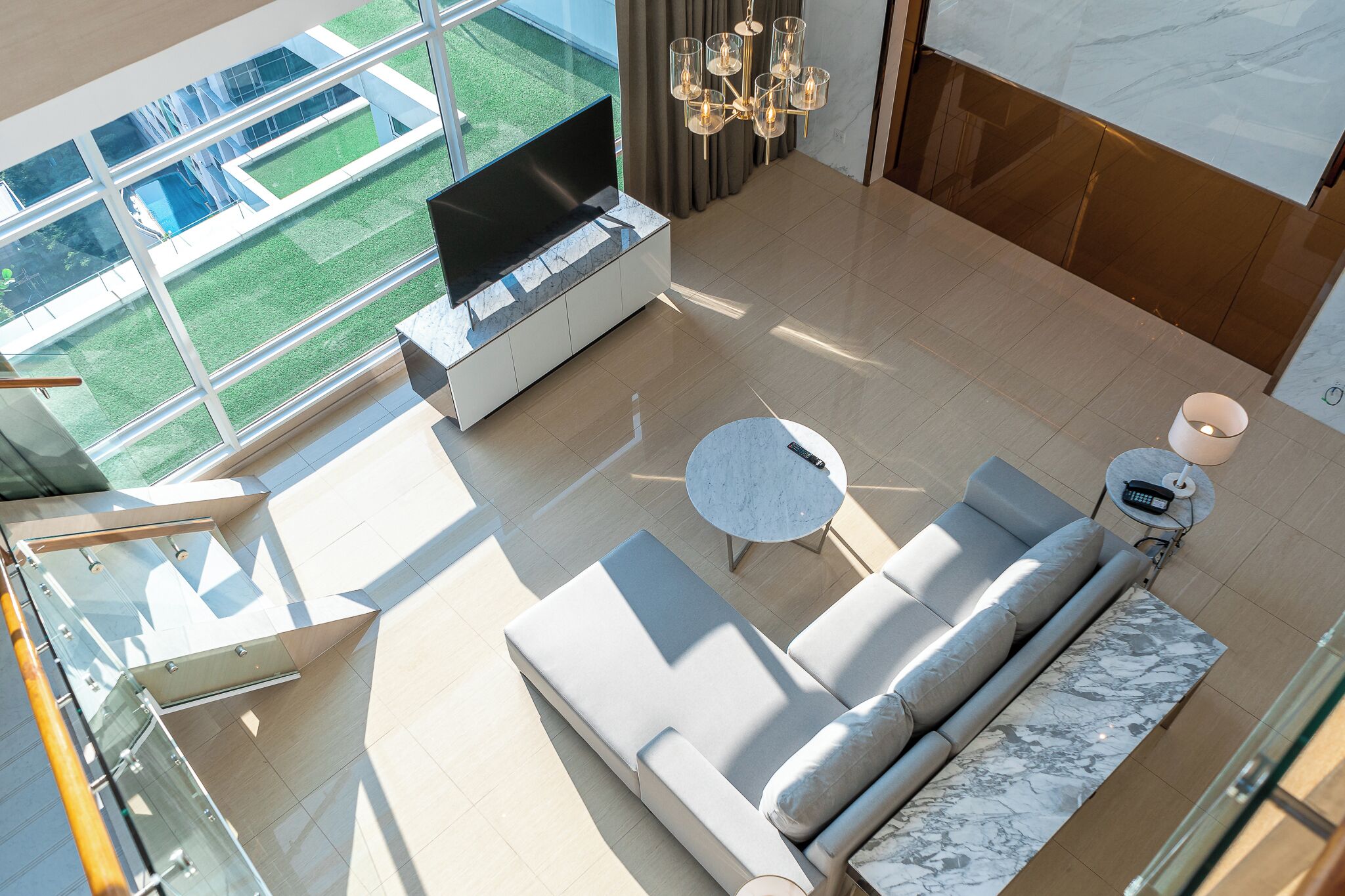 Un salon moderne doté d’un grand téléviseur, d’un canapé, d’une table basse et offrant une vue sur un espace extérieur verdoyant.