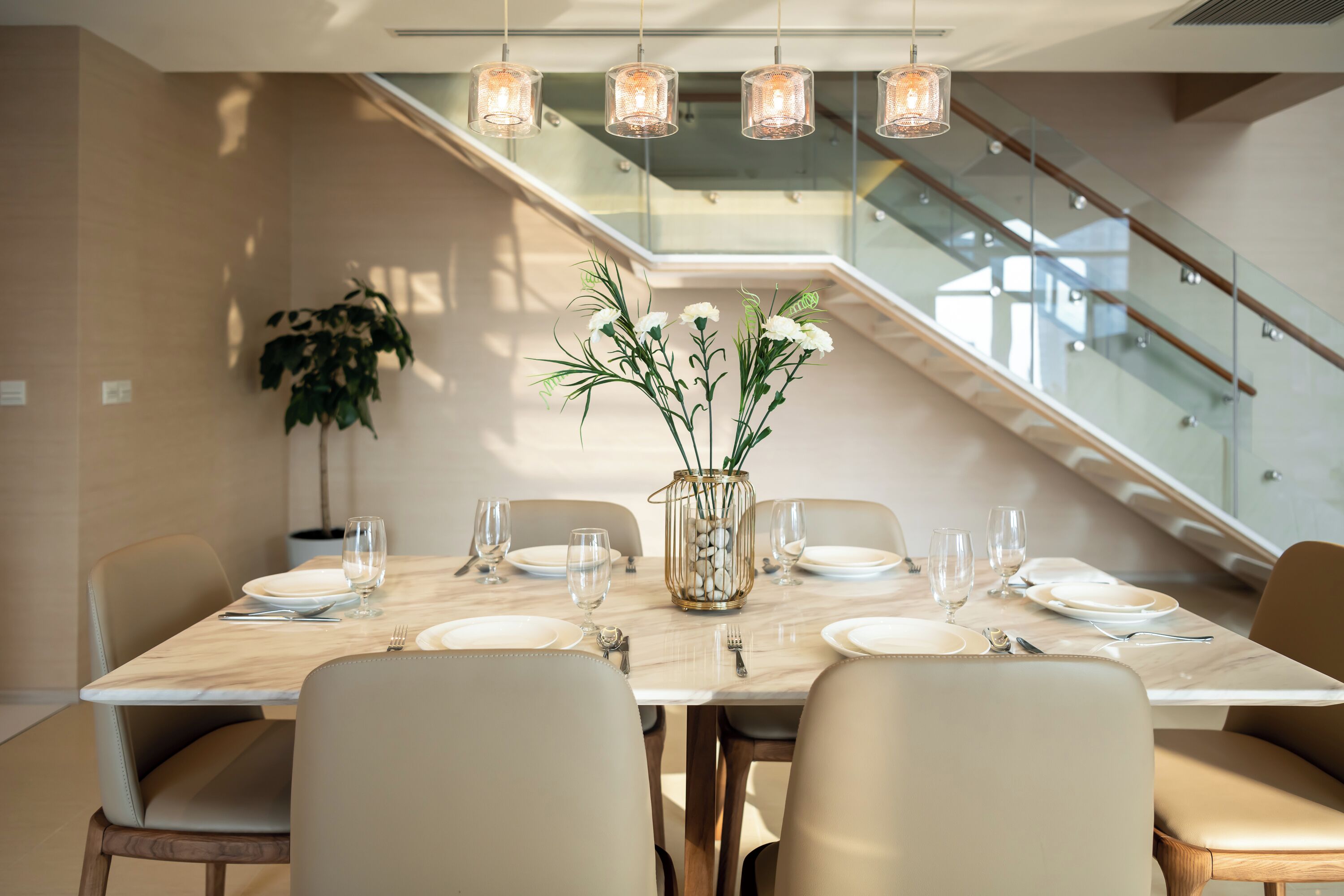 A modern dining area with a marble table, beige chairs, and a vase with flowers.