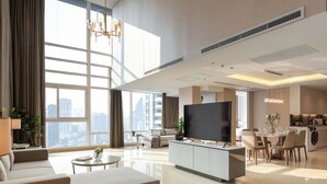 A spacious living room with a large TV, comfortable seating, a dining area, and a view of the city. - Jasmine 59 Hotel Thonglor Bangkok (Bangkok)
