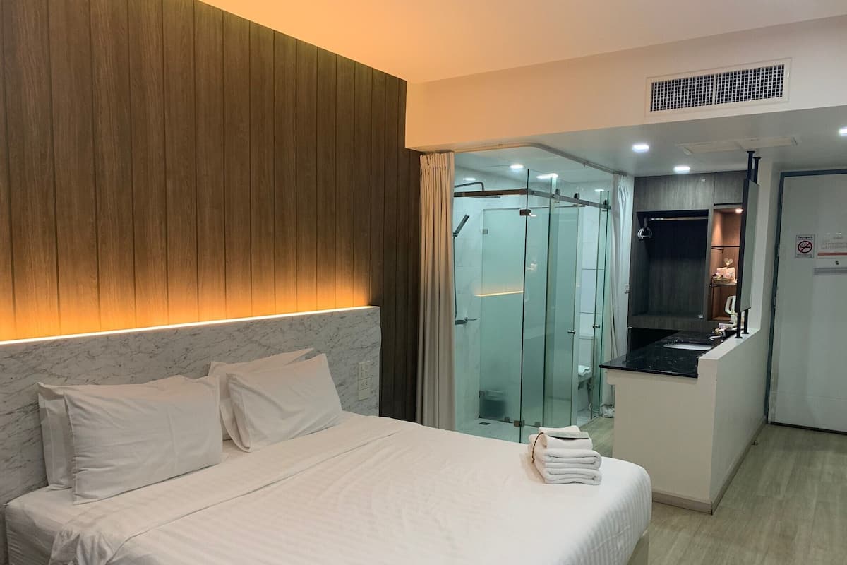 Habitación de hotel con cama, pared de paneles de madera, cabina de ducha de vidrio y una pequeña kitchenette.