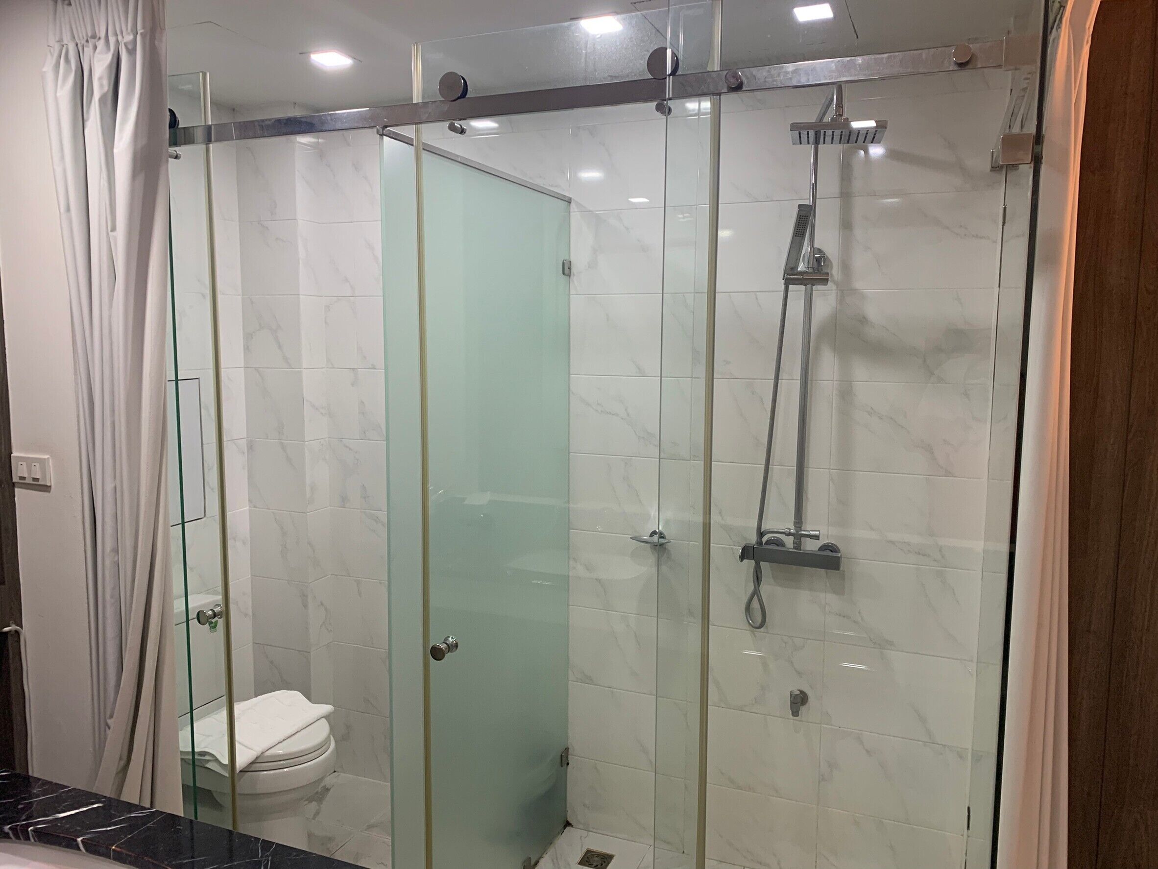 A glass-enclosed shower with a handheld showerhead and a wall-mounted faucet.
