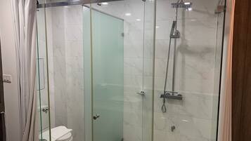 A glass-enclosed shower with a handheld showerhead and a wall-mounted faucet.
