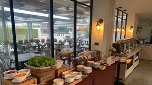 A buffet setup with various food items and a view of the outdoor seating area. - Phurinda Residence (Nong Khae)