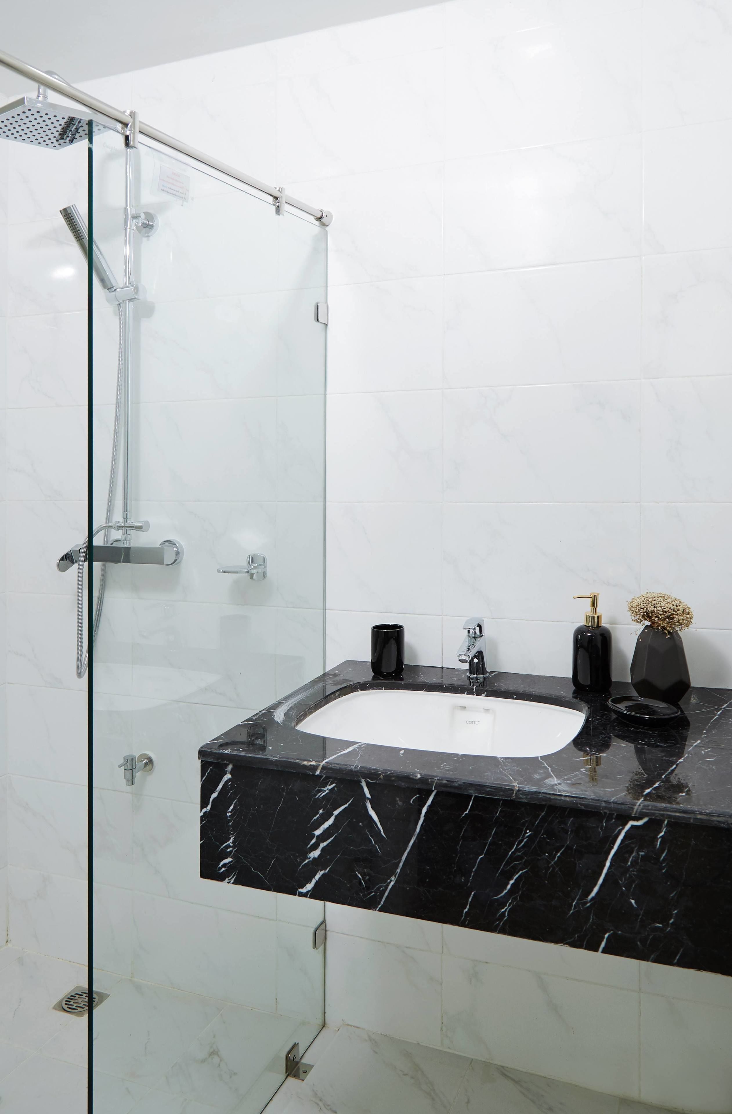 A modern bathroom with a glass-enclosed shower, a black marble sink, and a white tiled wall.