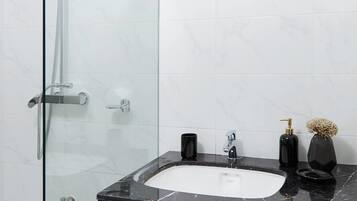 A modern bathroom with a glass-enclosed shower, a black marble sink, and a white tiled wall.