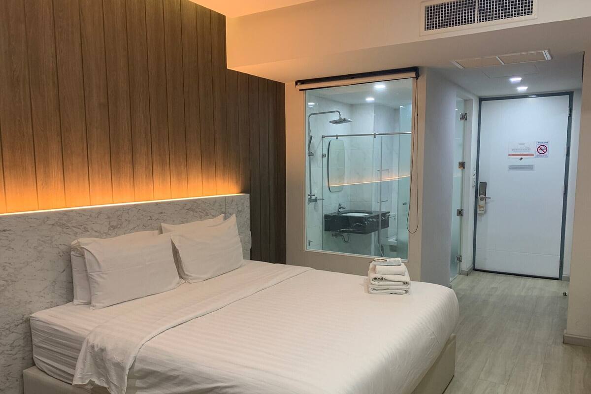 Habitación de hotel con cama, cabina de ducha de vidrio y puerta con letrero de no fumar.