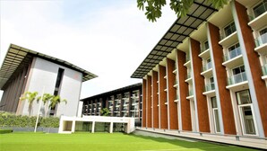 A modern building with a flat roof, large windows, and a green lawn in front. - Phurinda Residence (Nong Khae)