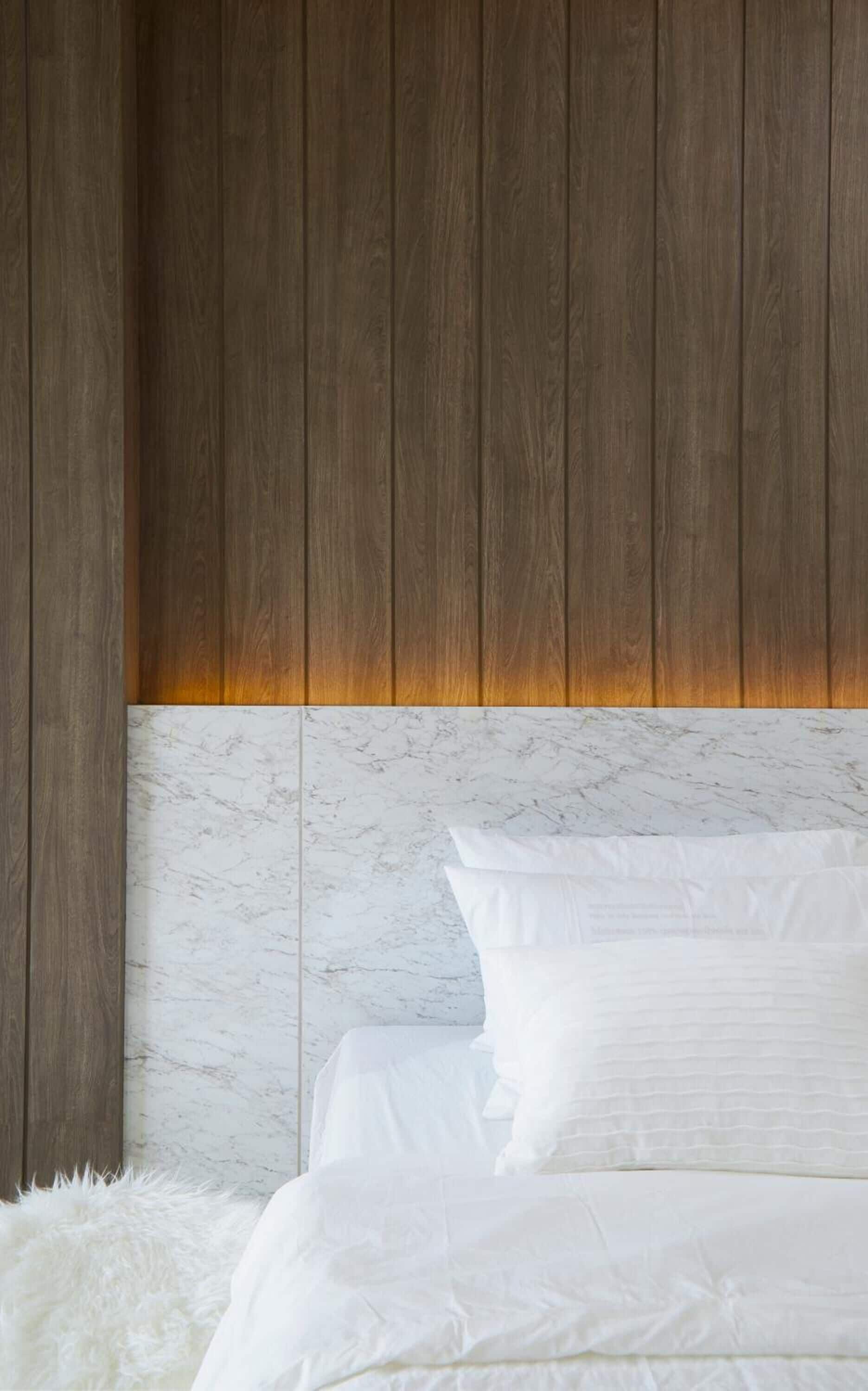 Un dormitorio con cabecera de madera, ropa de cama blanca y una alfombra mullida de color blanco.
