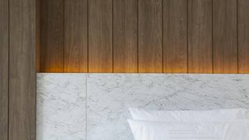 Un dormitorio con cabecera de madera, ropa de cama blanca y una alfombra mullida de color blanco.