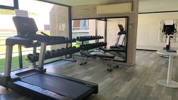Un gimnasio con cinta de correr, mancuernas y banco.