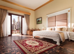 A spacious bedroom with a large bed, a red and gold patterned rug, and a view of a building through a glass door.