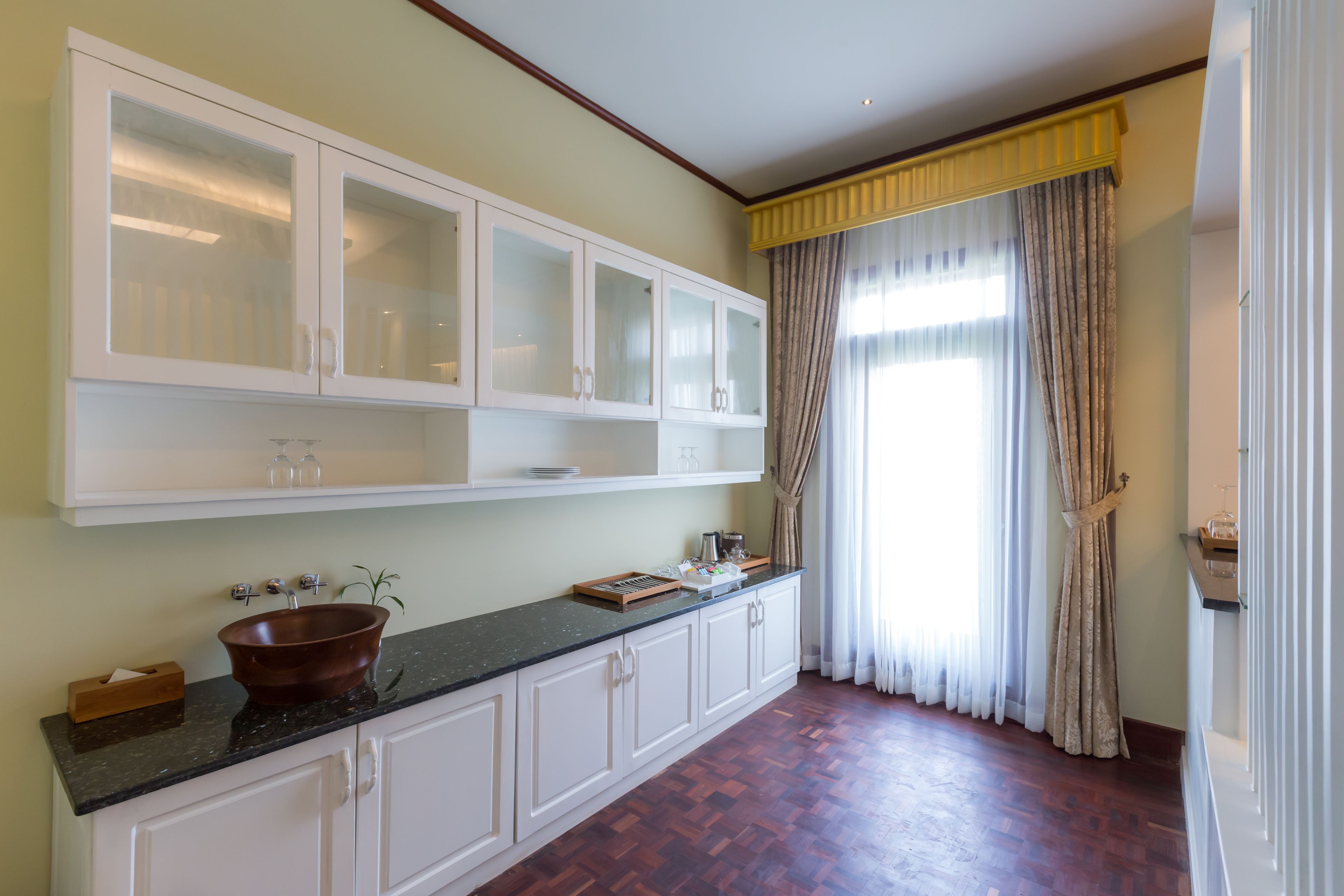 A kitchen with a wooden countertop, white cabinets, and a large window with curtains.