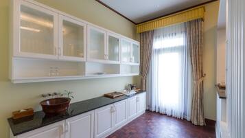 A kitchen with a wooden countertop, white cabinets, and a large window with curtains.