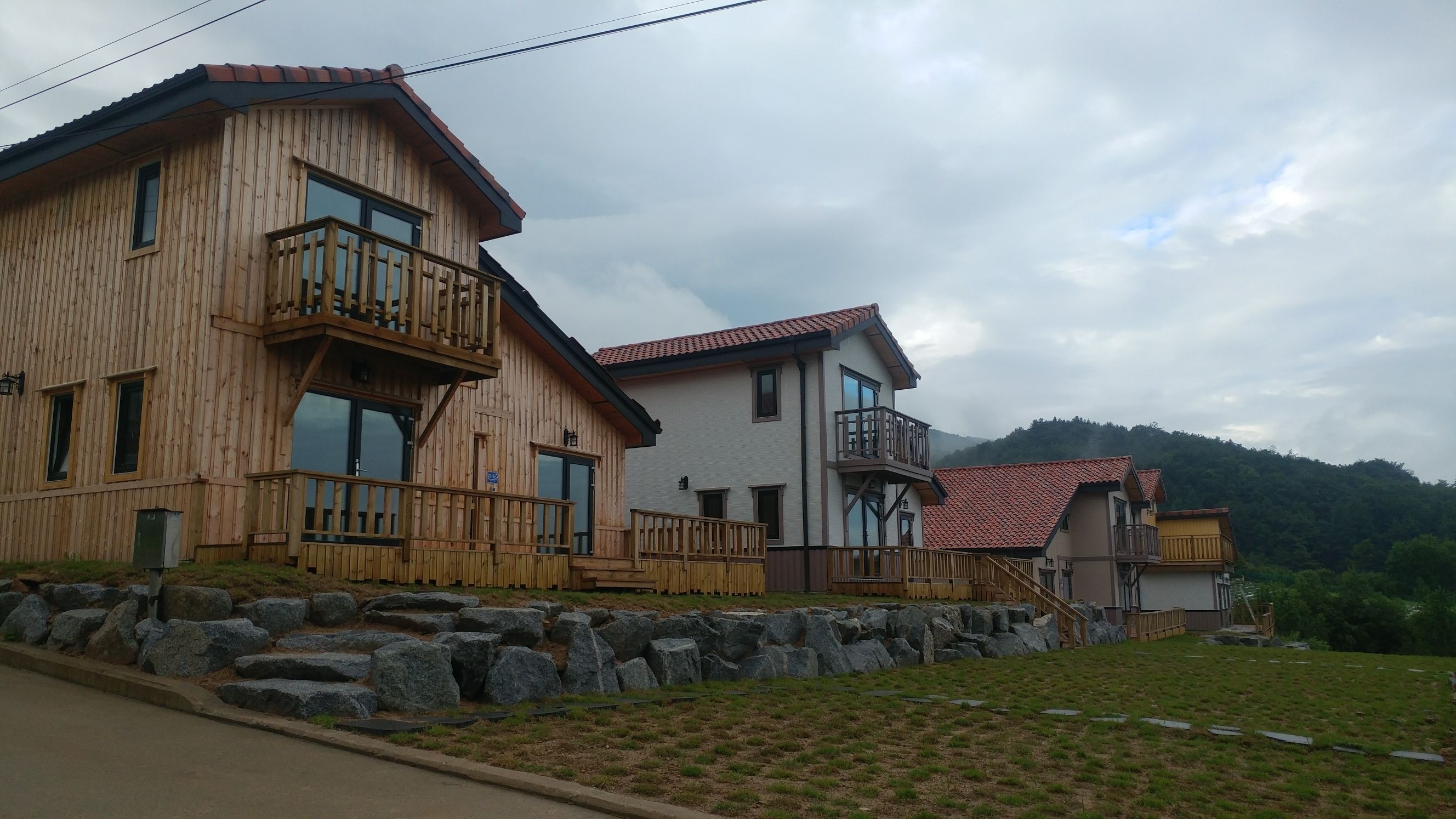 Una cabaña de madera con un balcón, un muro de piedra y una zona verde.