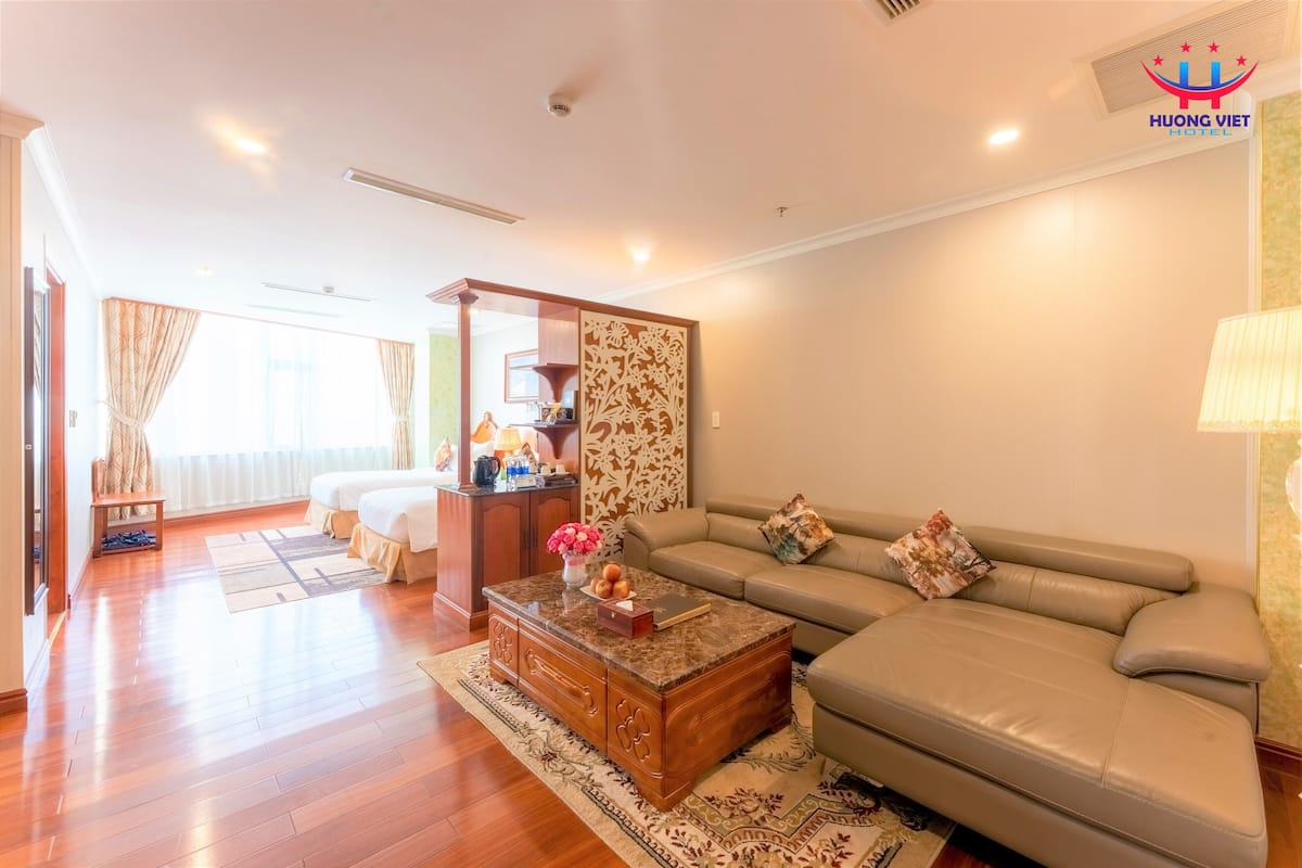 A hotel room with a wooden floor, a beige sofa, a coffee table, and a bed with a headboard.