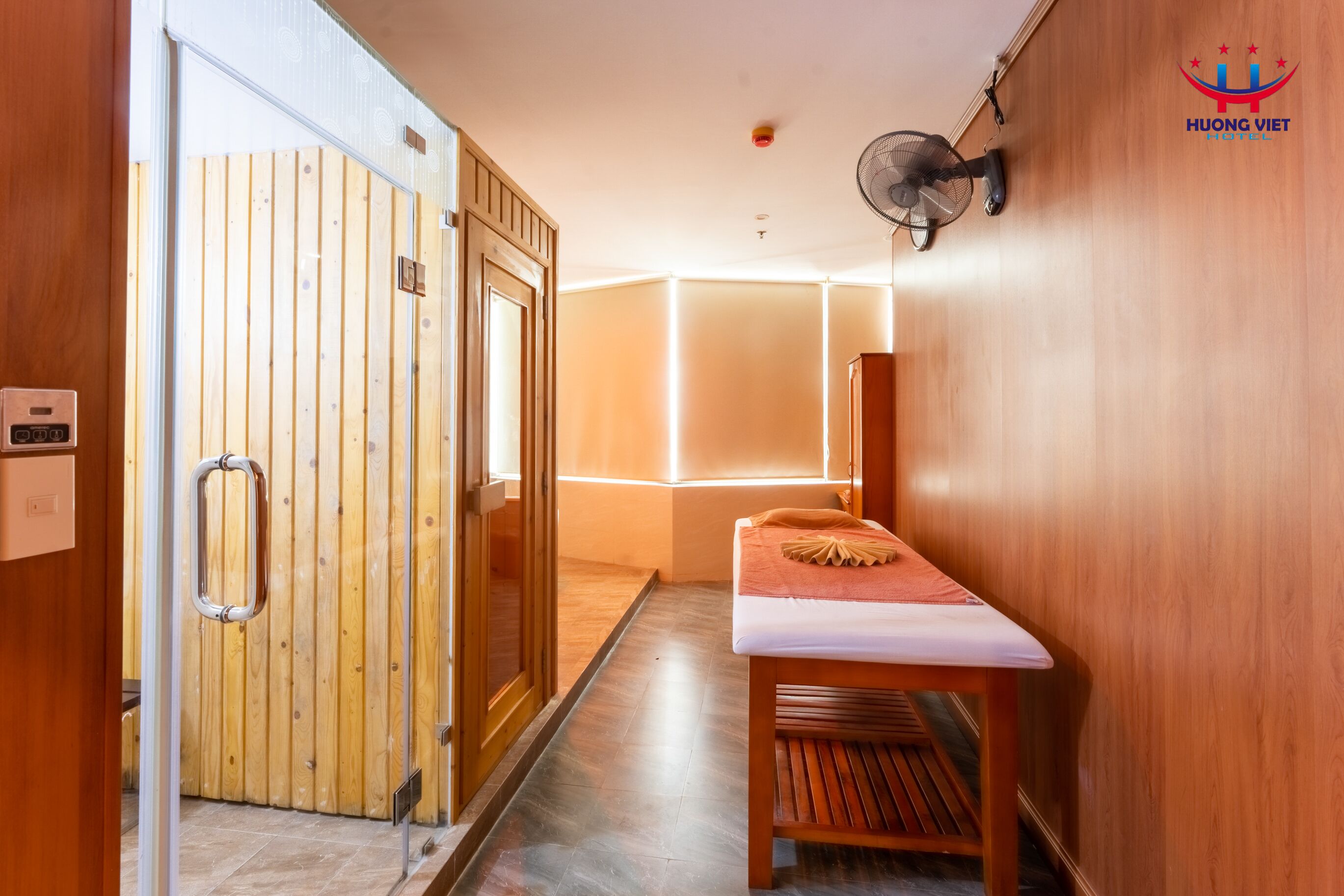 Une pièce en bois avec une table de massage, un ventilateur et une porte en bois.