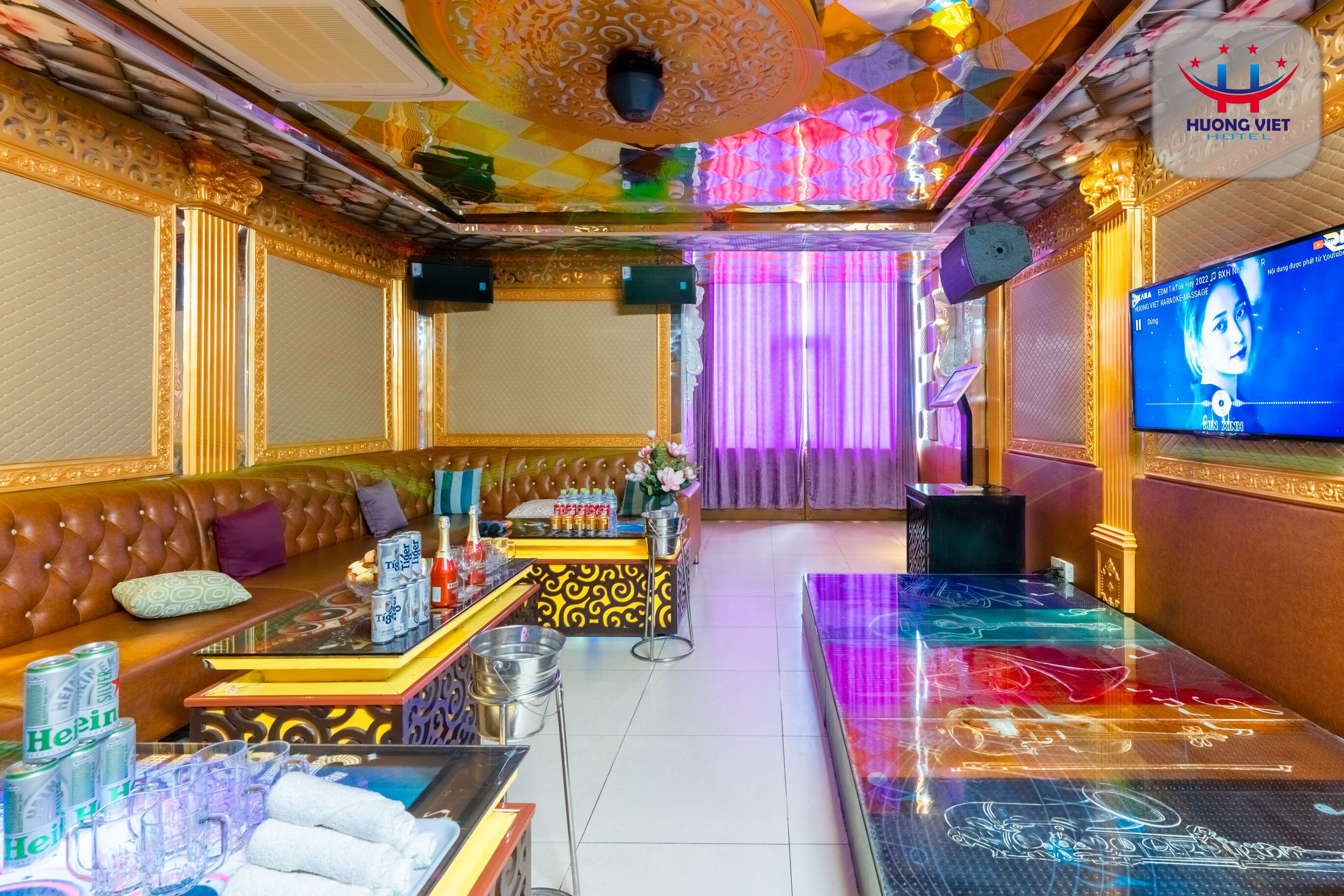 A luxurious hotel room with a plush brown sofa, a minibar, and a television displaying a woman.