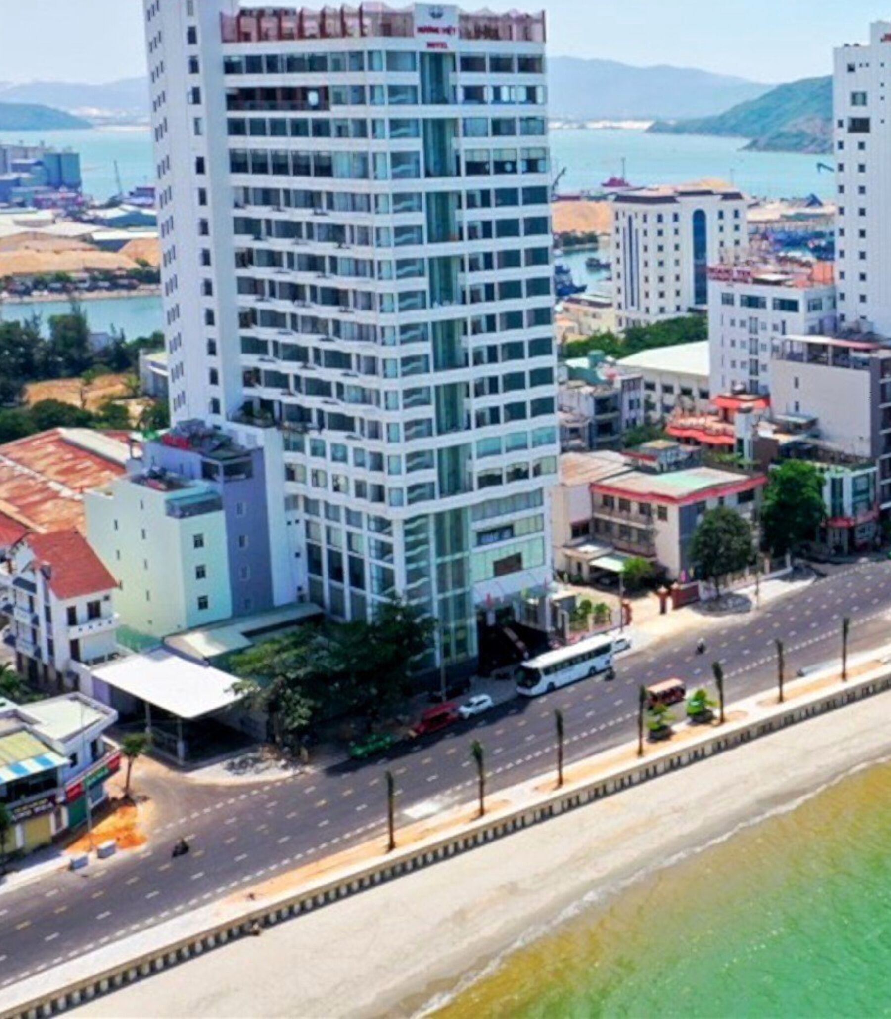 Un hotel moderno de gran altura, con varios pisos, una entrada destacada y vistas del entorno urbano, incluyendo una playa y otros edificios.