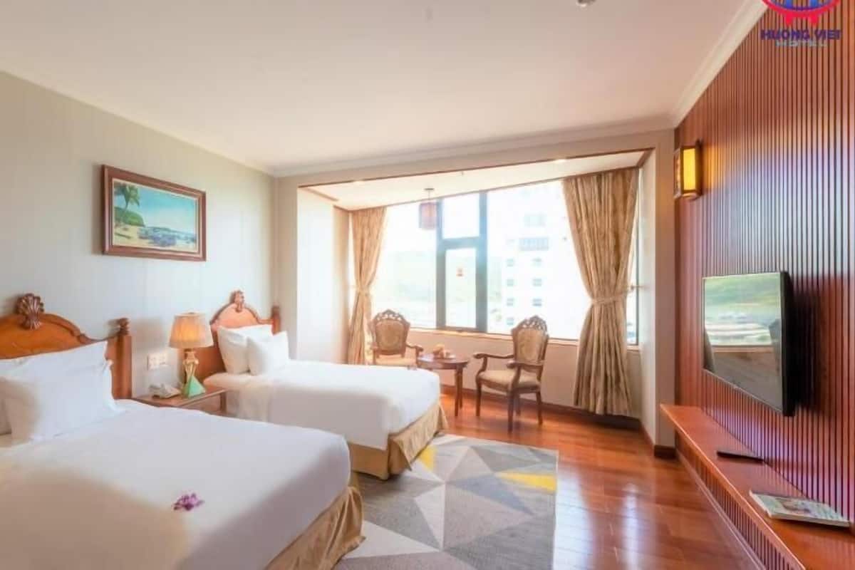 A hotel room with two beds, a TV, a painting, and a view of the city.