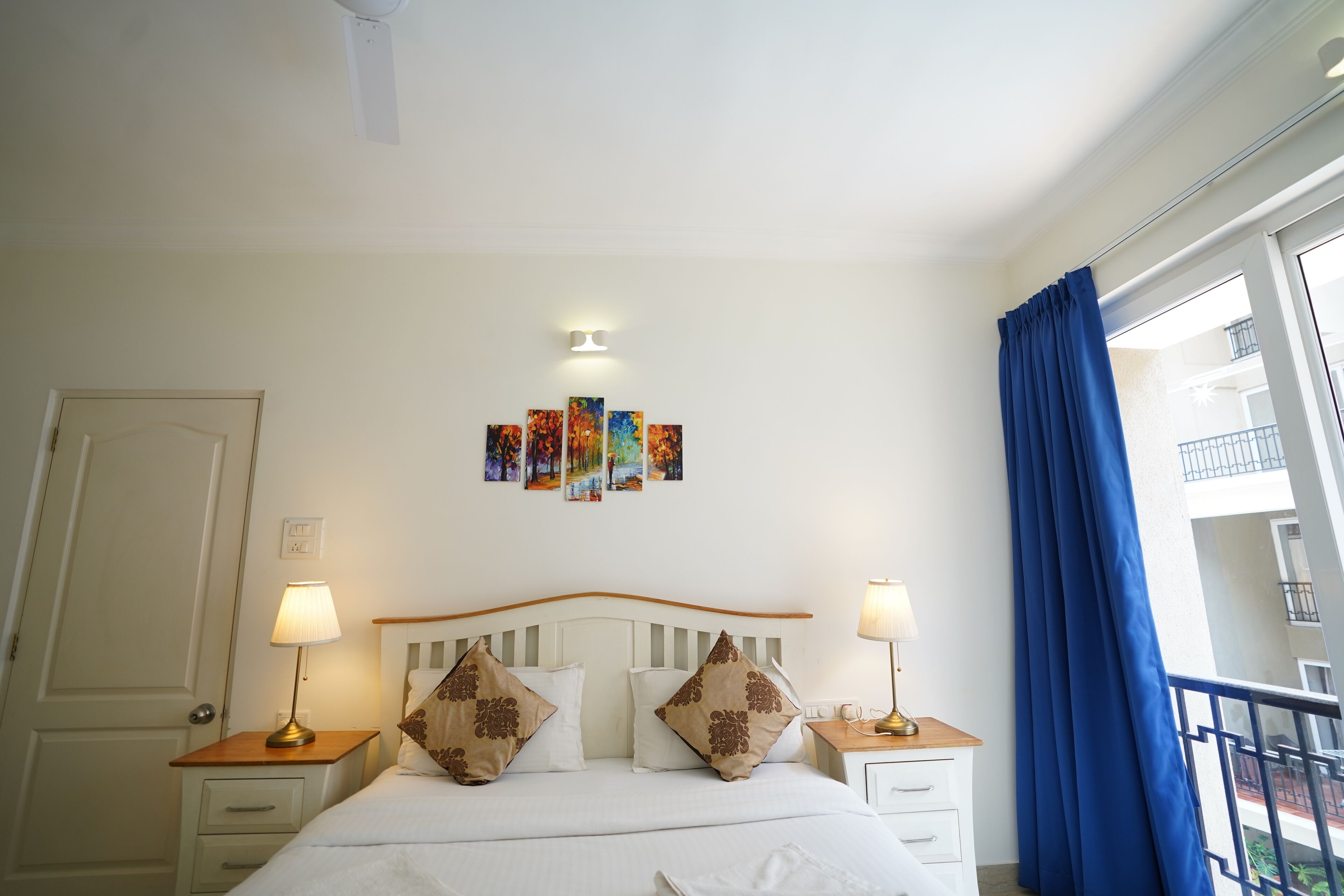 Habitación de hotel impecable con cama, lámparas de noche, una obra de arte en la pared y vistas al balcón exterior.
