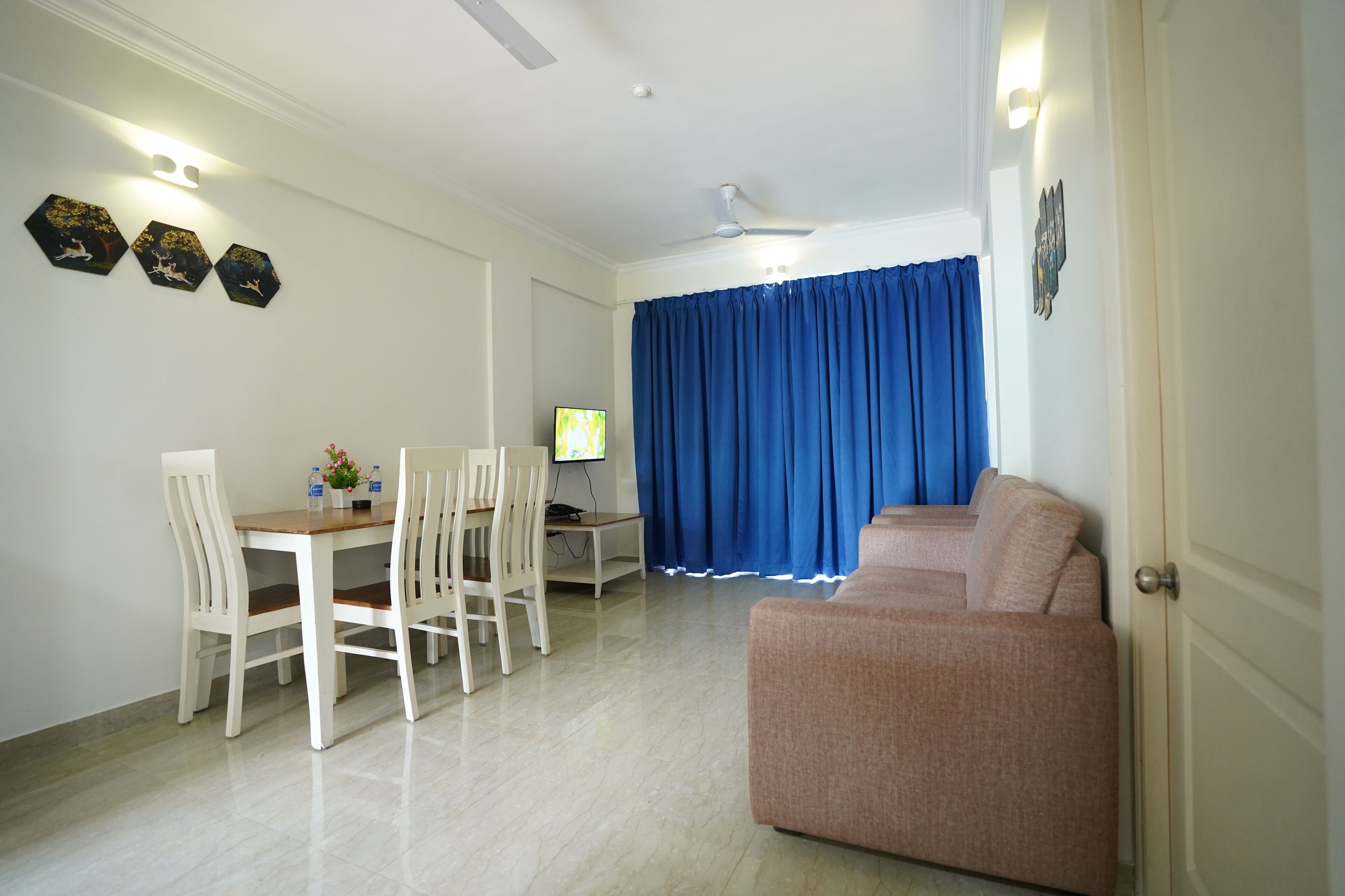 A living room with a beige sofa, a dining table with chairs, a TV, and a ceiling fan.