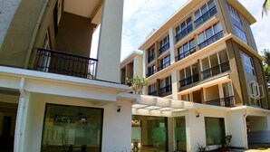 Un immeuble à plusieurs étages doté de balcons, de grandes fenêtres et d’une cour pavée agrémentée de plantes en pot.