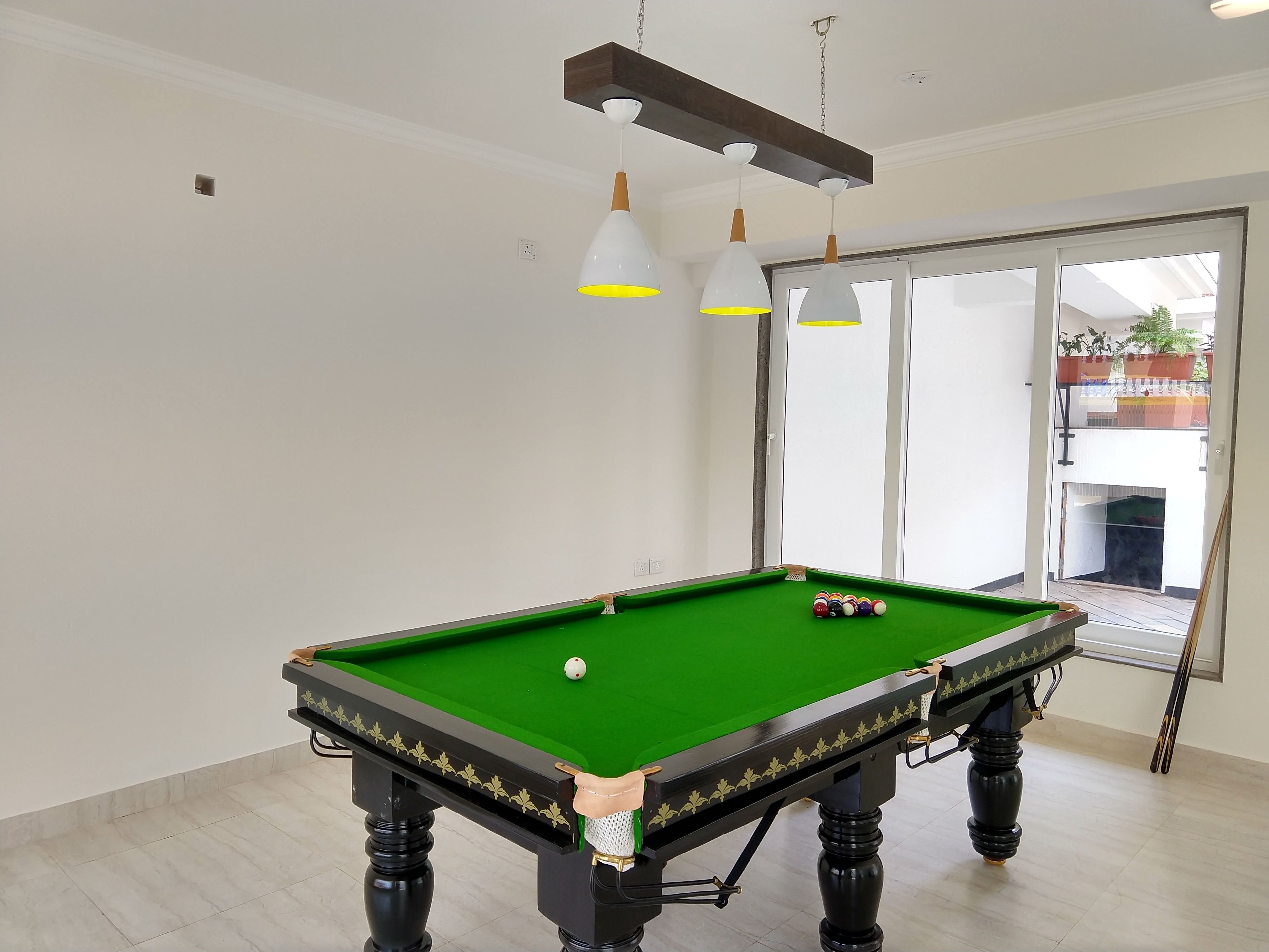 A pool table with a green felt surface, positioned in a room with white walls and a large window.