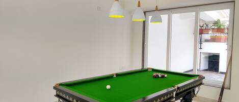 A pool table with a green felt surface, positioned in a room with white walls and a large window.
