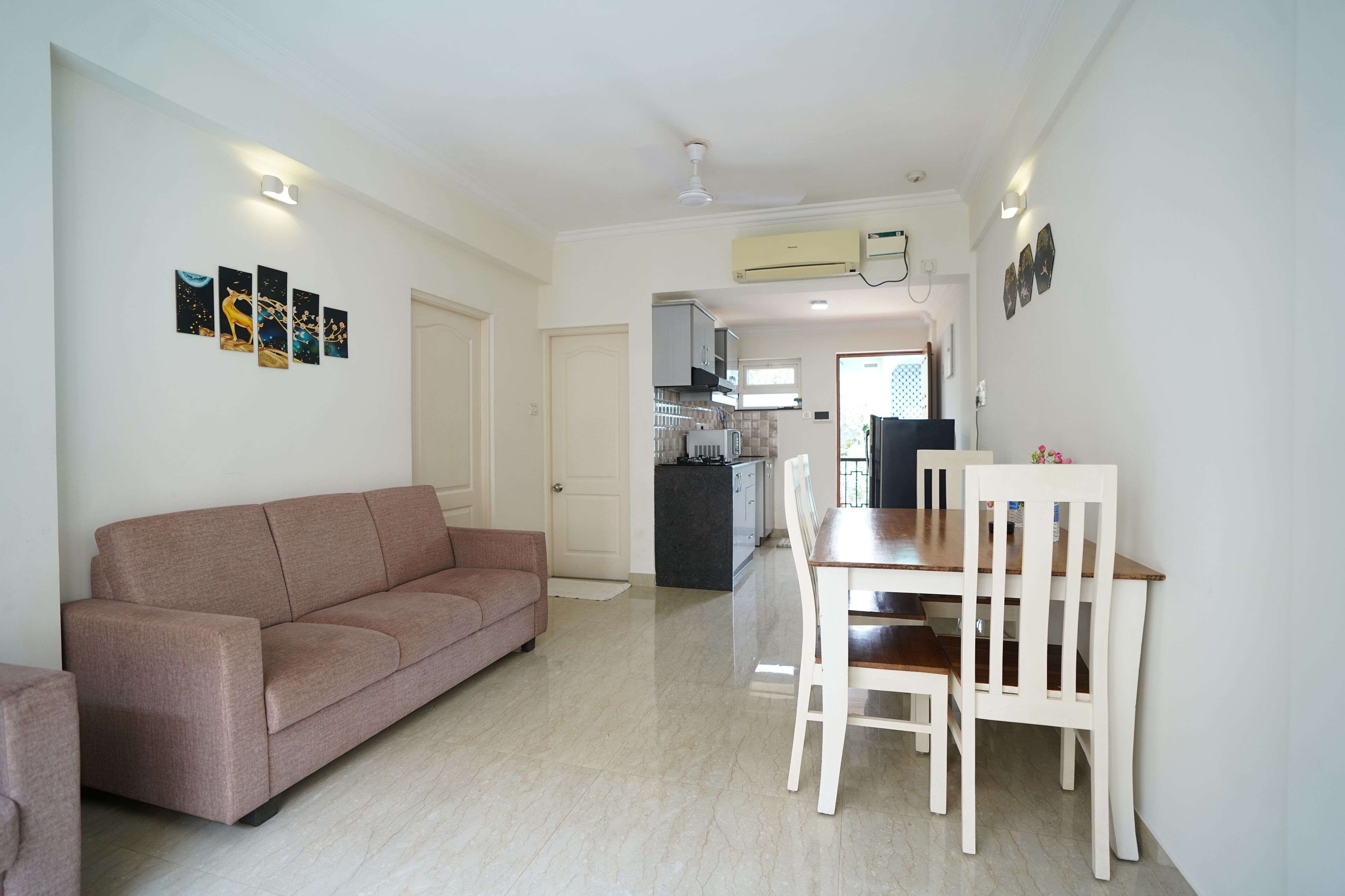A modern living room with a sofa and a dining table with chairs. There is a kitchen area in the background.