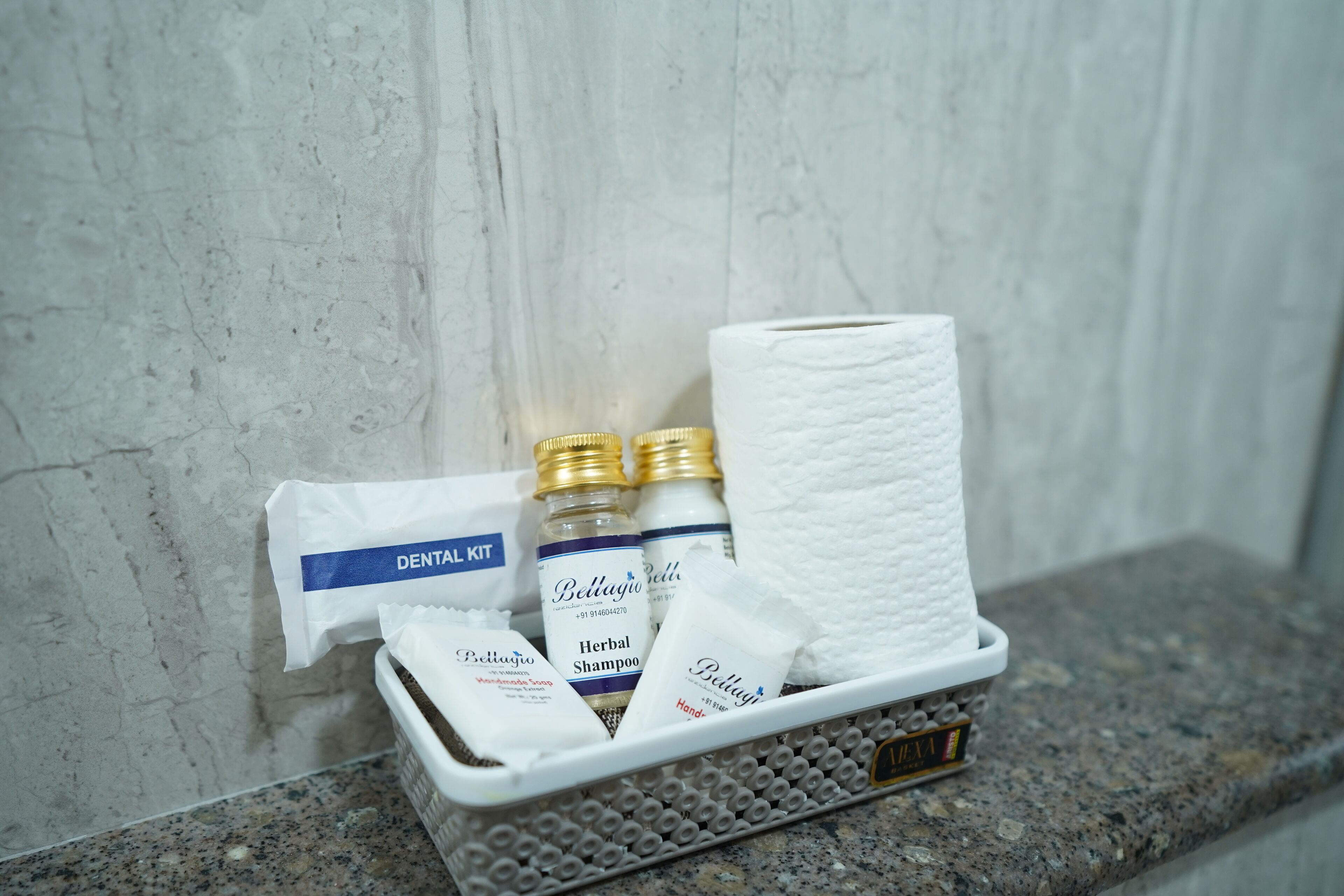 A dental kit, two bottles of Bellajugo Herbal Shampoo, a pack of tissues, and a small container on a granite countertop.