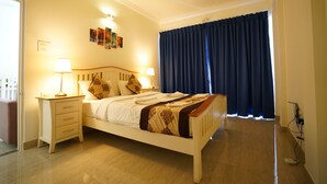 Une chambre à coucher avec un lit, des lampes de chevet, une table de chevet, une fenêtre avec des rideaux et des œuvres d’art accrochées au mur.